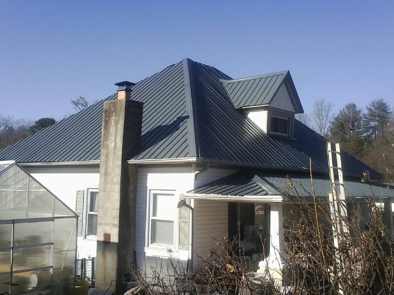 Dark blue standing seam metal roof on a white farmhouse with dormer — Slate & Tile Roof Repair by Roofing Brothers in Boyden