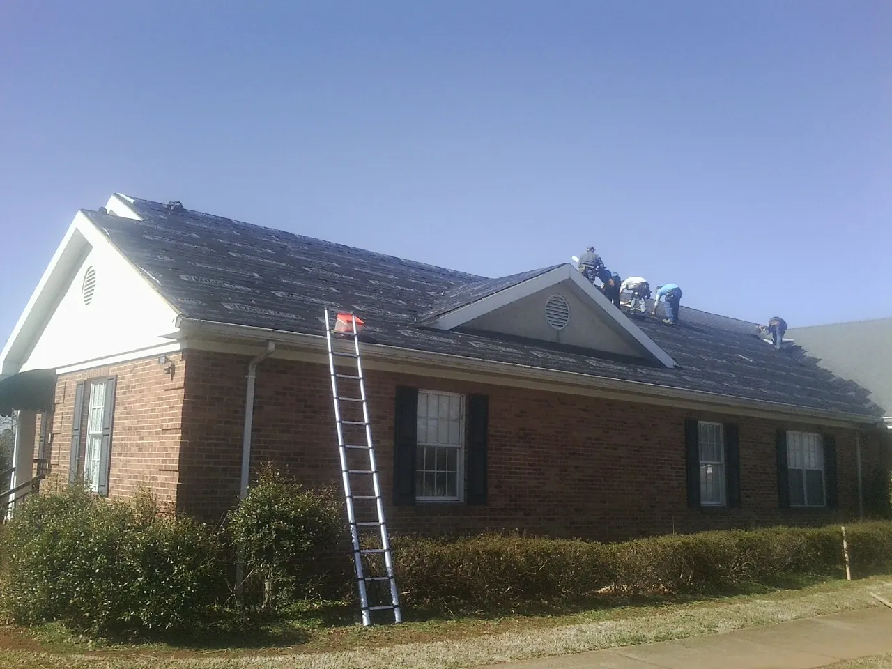 Crew tearing shingles off a brick ranch roof with a ladder set — Emergency Roof Repair work by our crew in Boyden