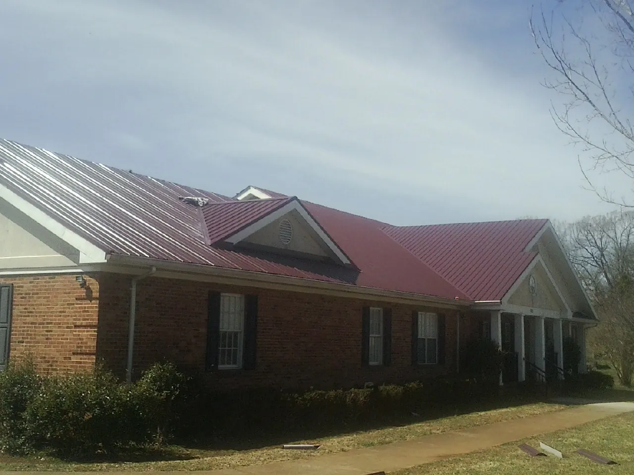 Red metal roof with gabled entries on a long brick building, from a Hail Damage Roof Repair job in Boyden