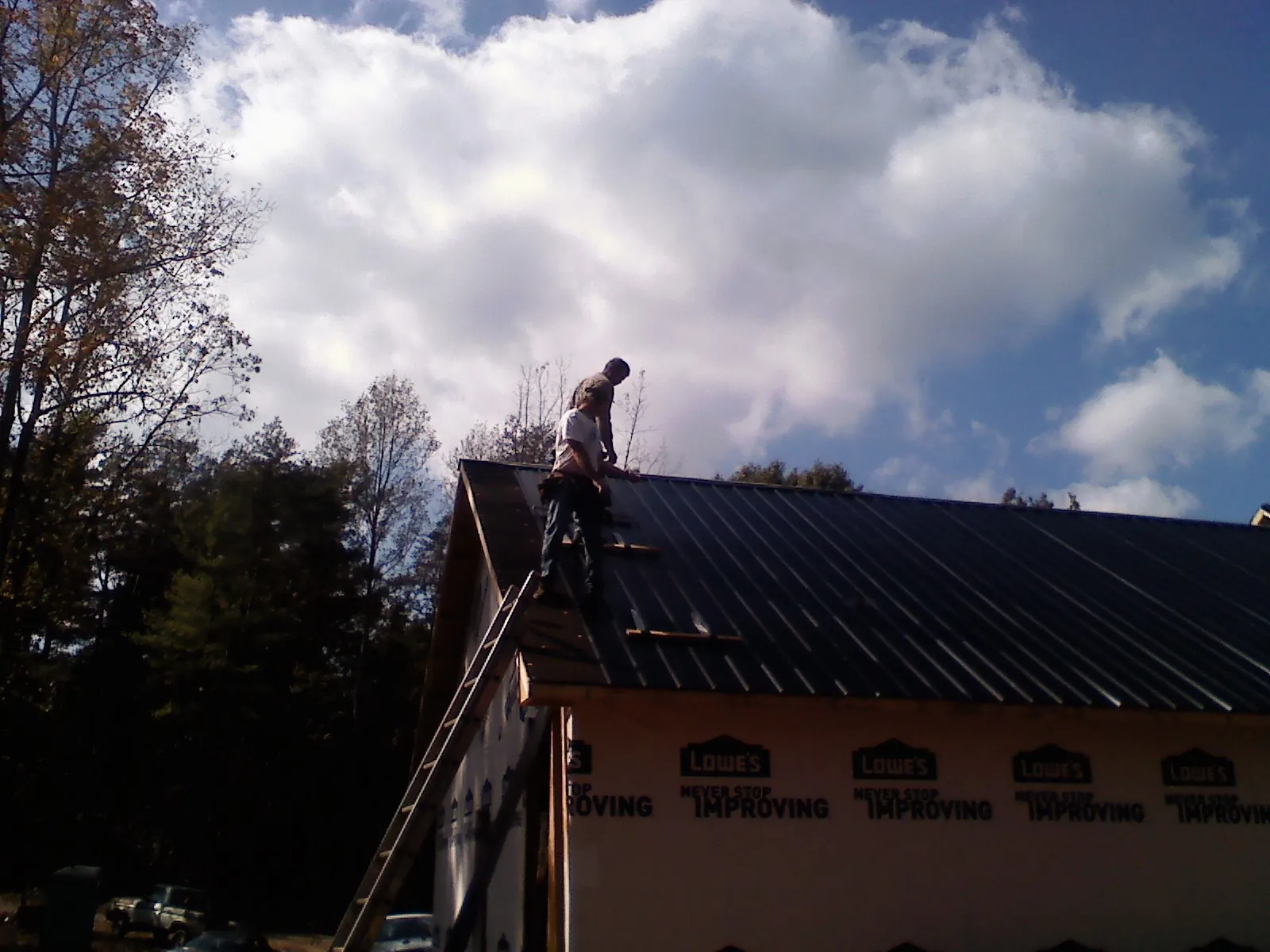 Roofer fastening dark metal panels high against a cloudy sky, from a Roof Inspection job in Boyden