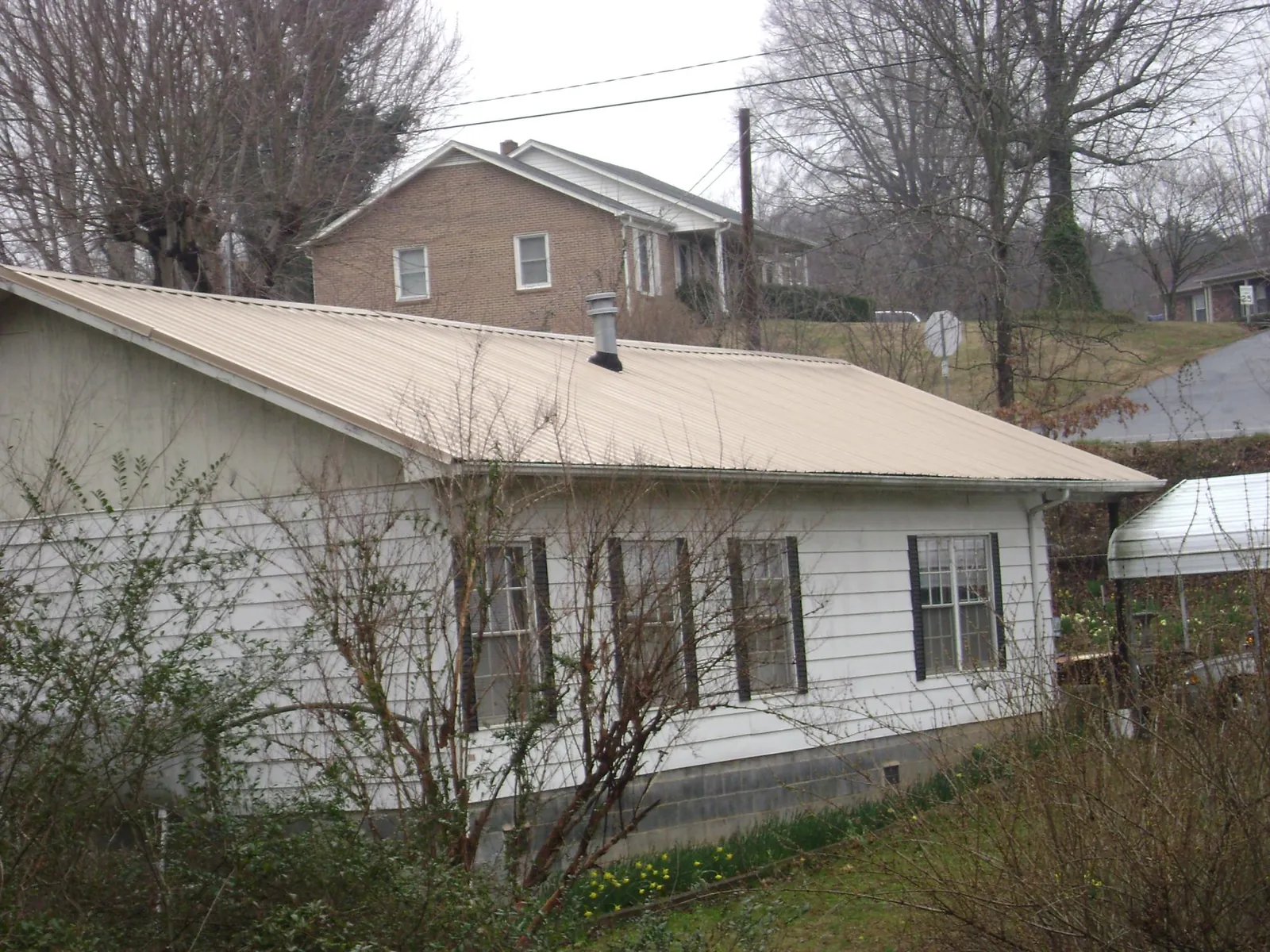 Tan metal roof on a white sided house set into a hillside — Commercial Roofing by Roofing Brothers in Boyden