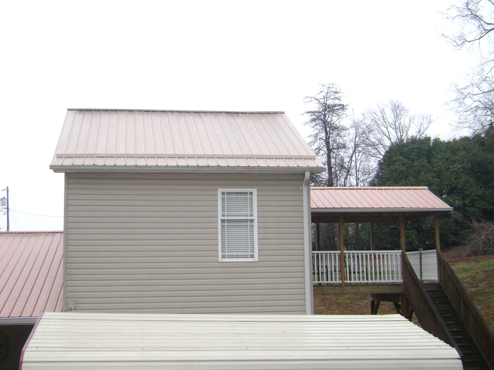 Tan metal roofs on a two story addition and attached porch, from a Roof Replacement job in Boyden